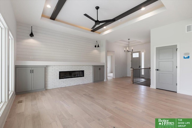 unfurnished living room with light wood-type flooring, a fireplace, a tray ceiling, and ceiling fan with notable chandelier