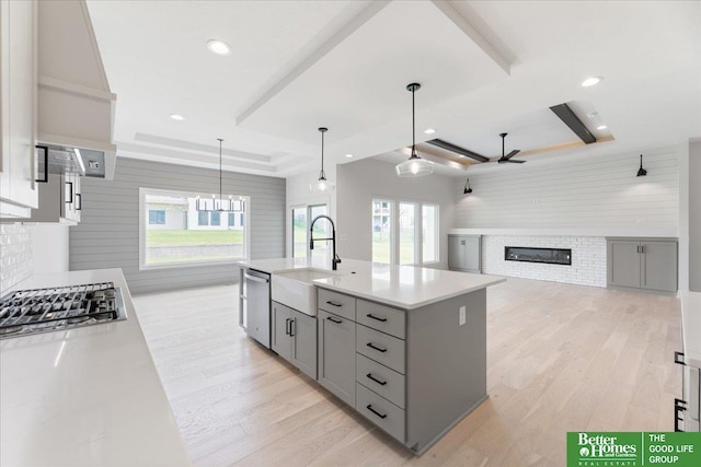 kitchen featuring a tray ceiling, a glass covered fireplace, a sink, and gray cabinetry