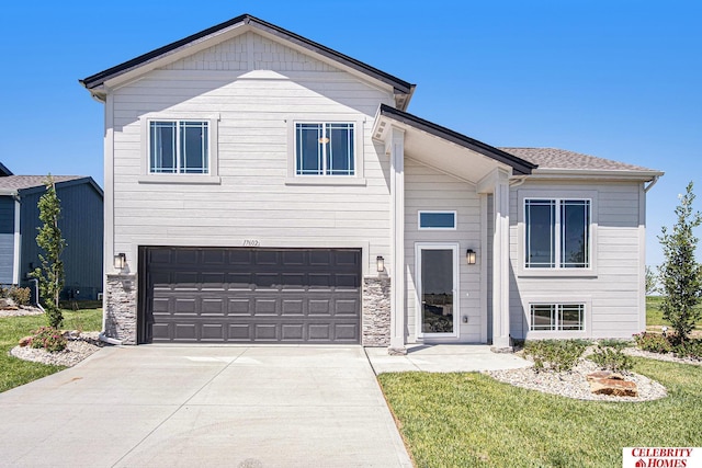 view of front of property featuring a garage, stone siding, driveway, and a front yard