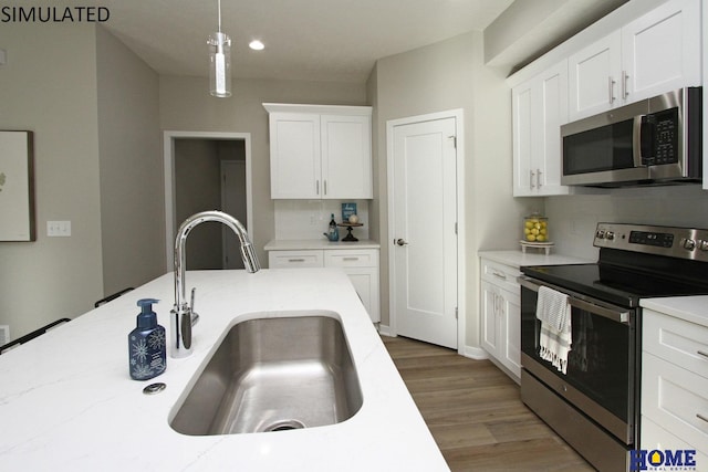 kitchen featuring wood finished floors, hanging light fixtures, stainless steel appliances, white cabinetry, and a sink