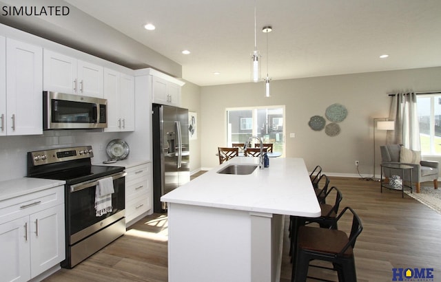 kitchen with a center island with sink, appliances with stainless steel finishes, wood finished floors, a sink, and backsplash