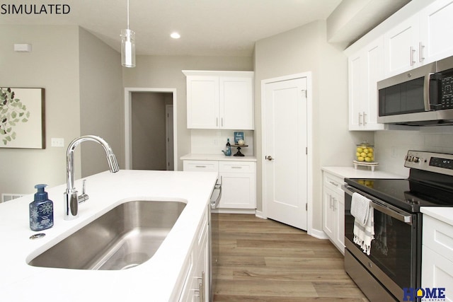 kitchen with stainless steel appliances, wood finished floors, a sink, white cabinetry, and backsplash