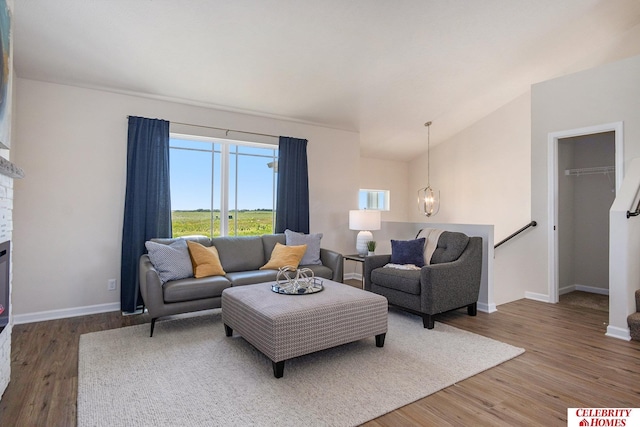 living area featuring vaulted ceiling, baseboards, wood finished floors, and a chandelier