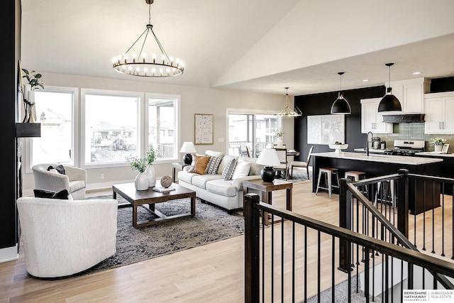 living area with lofted ceiling, light wood-style floors, baseboards, and a chandelier