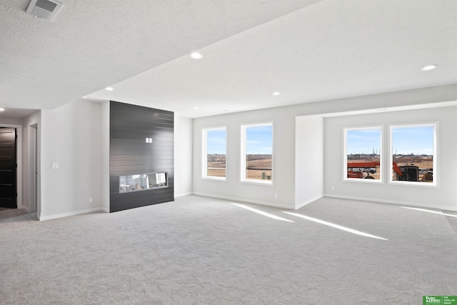 unfurnished living room with a healthy amount of sunlight, a large fireplace, carpet, and visible vents