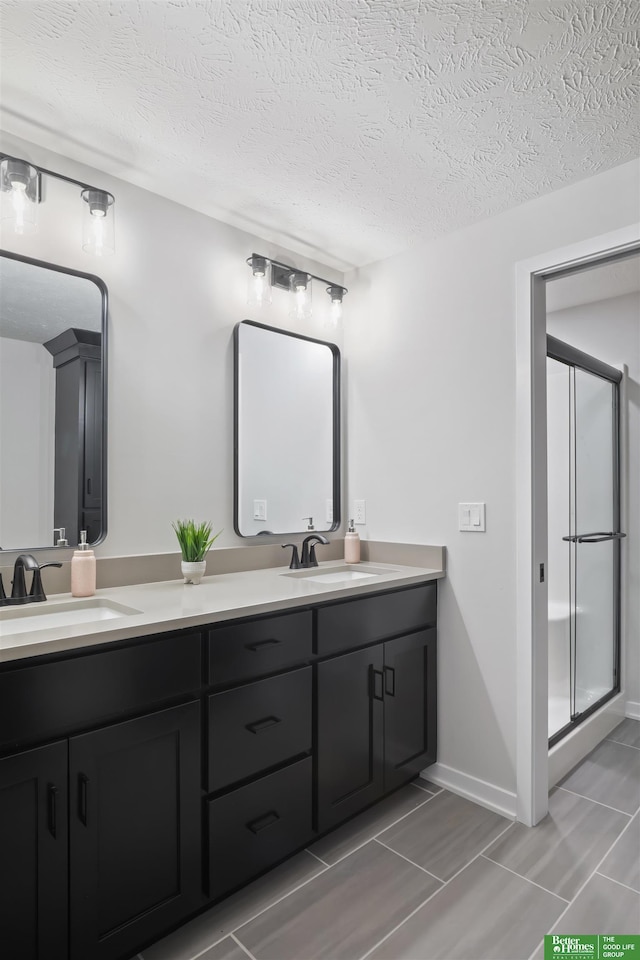 bathroom featuring a textured ceiling, double vanity, a sink, and a shower stall