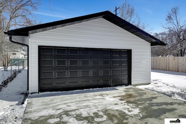 snow covered garage featuring a garage and fence