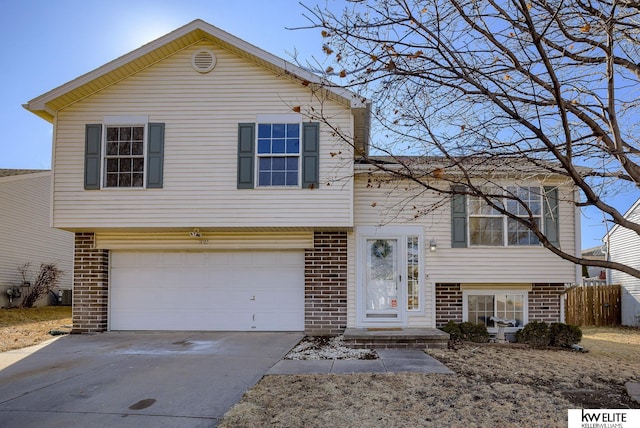 tri-level home with concrete driveway, brick siding, an attached garage, and fence