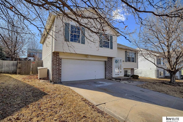 split level home with a garage, concrete driveway, brick siding, and fence