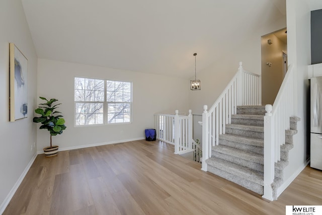 staircase with a notable chandelier, high vaulted ceiling, wood finished floors, and baseboards