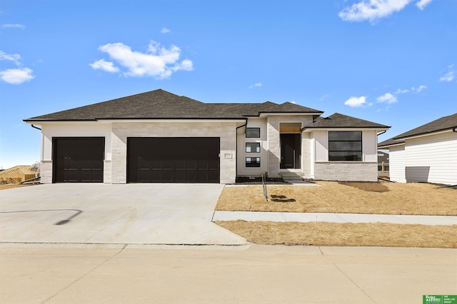 prairie-style house featuring a garage, stone siding, a shingled roof, and concrete driveway