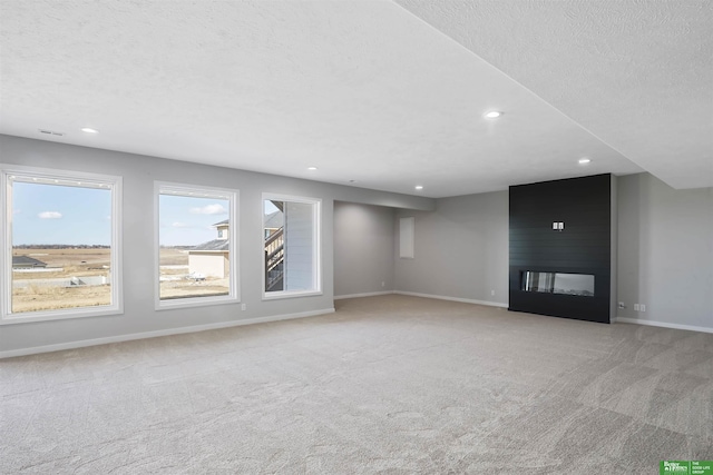 unfurnished living room with a textured ceiling, recessed lighting, light colored carpet, a fireplace, and baseboards