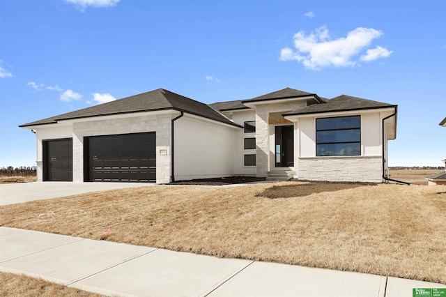 prairie-style home with an attached garage, stone siding, driveway, roof with shingles, and stucco siding