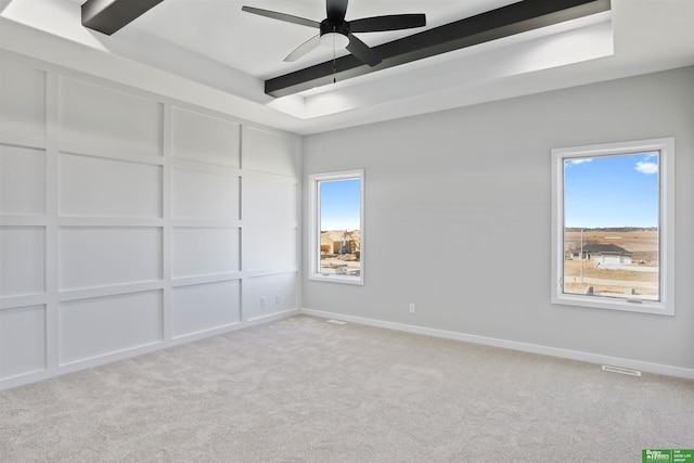 carpeted empty room featuring a healthy amount of sunlight, a decorative wall, and beam ceiling