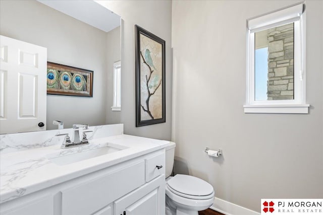 bathroom featuring toilet, plenty of natural light, baseboards, and vanity