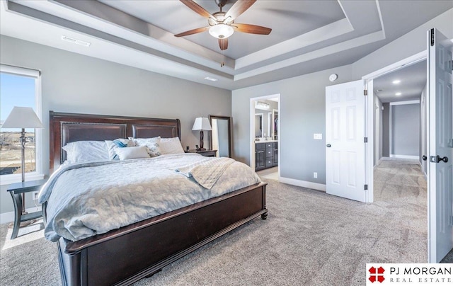 carpeted bedroom with baseboards, visible vents, a raised ceiling, ceiling fan, and ensuite bathroom