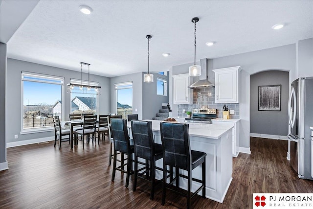 kitchen featuring dark wood-style flooring, decorative backsplash, appliances with stainless steel finishes, white cabinets, and wall chimney range hood