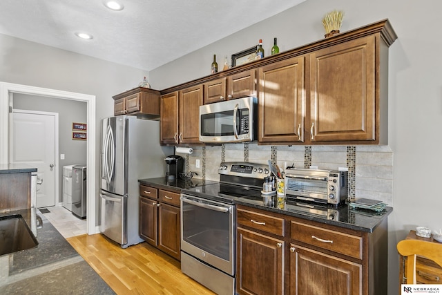 kitchen with light wood-style flooring, washing machine and dryer, tasteful backsplash, and stainless steel appliances