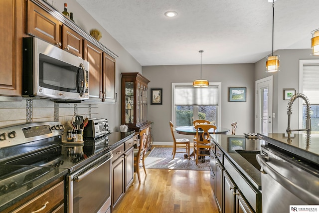 kitchen featuring light wood-style flooring, a toaster, appliances with stainless steel finishes, decorative light fixtures, and tasteful backsplash