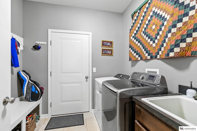 clothes washing area with baseboards, laundry area, light tile patterned flooring, washer and dryer, and a sink