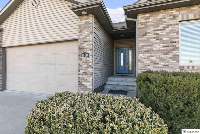 property entrance with brick siding, an attached garage, and driveway