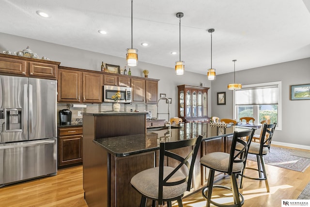 kitchen with a kitchen bar, light wood-style flooring, an island with sink, and appliances with stainless steel finishes