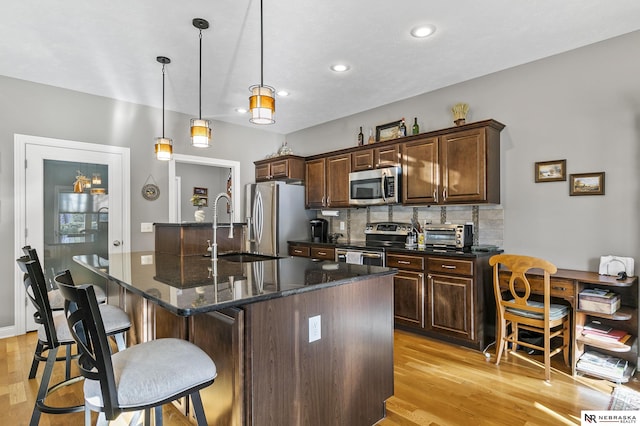 kitchen with a kitchen bar, decorative backsplash, light wood-style flooring, and appliances with stainless steel finishes