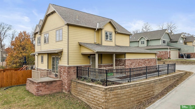 view of front of house with brick siding, a shingled roof, and fence