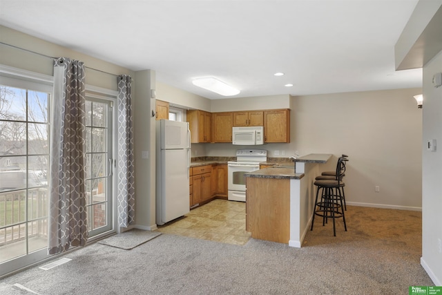 kitchen featuring white appliances, light carpet, a peninsula, and a kitchen bar