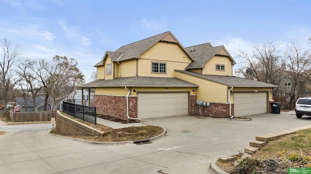 view of front of home with a shingled roof, concrete driveway, brick siding, and fence