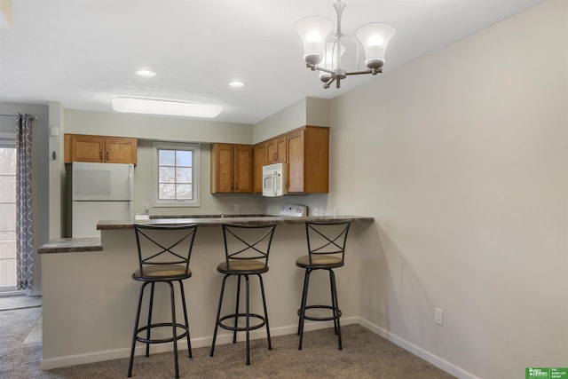 kitchen with brown cabinetry, dark countertops, white appliances, and a peninsula