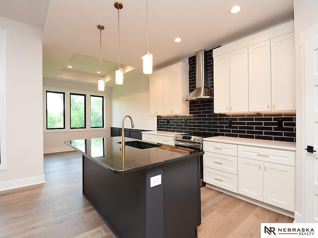 kitchen featuring a sink, wall chimney range hood, decorative backsplash, light wood finished floors, and stainless steel range with electric stovetop