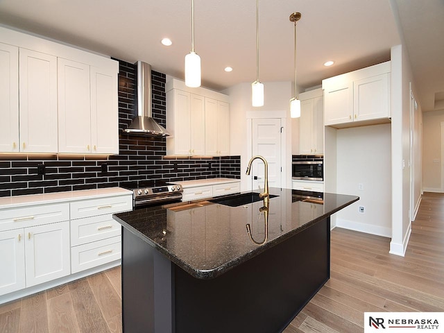 kitchen with tasteful backsplash, light wood-style floors, stainless steel appliances, wall chimney range hood, and a sink