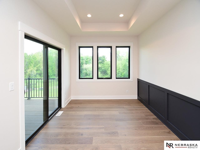 empty room featuring light wood-style flooring, a decorative wall, recessed lighting, wainscoting, and a tray ceiling