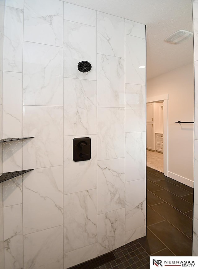 full bath with baseboards, visible vents, and tiled shower