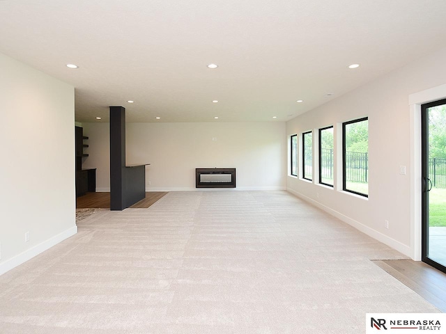 unfurnished living room featuring recessed lighting, light colored carpet, and plenty of natural light