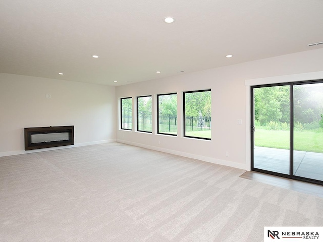 unfurnished living room with recessed lighting, visible vents, a glass covered fireplace, and light colored carpet