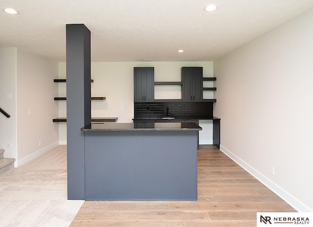 kitchen with a peninsula, a sink, light wood-type flooring, open shelves, and backsplash