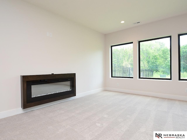 unfurnished living room featuring carpet floors, plenty of natural light, a glass covered fireplace, and visible vents