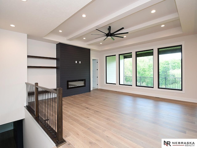 living room featuring light wood-type flooring, a fireplace, a tray ceiling, and beam ceiling