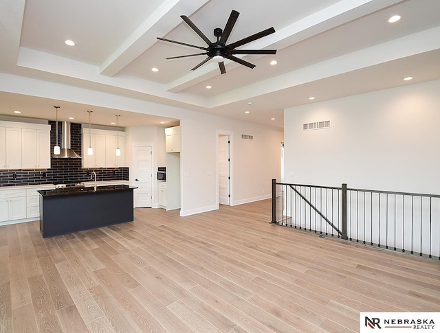 kitchen with light wood finished floors, visible vents, backsplash, open floor plan, and wall chimney exhaust hood