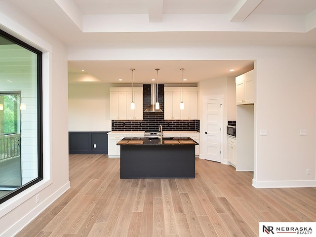 kitchen featuring light wood-style flooring, white cabinets, wall chimney range hood, and decorative backsplash