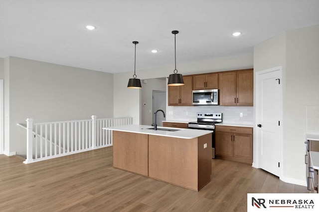 kitchen featuring a sink, light countertops, appliances with stainless steel finishes, light wood finished floors, and tasteful backsplash