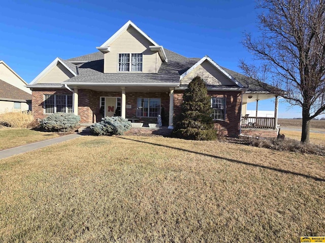 view of front of home with a shingled roof, a front yard, covered porch, and brick siding