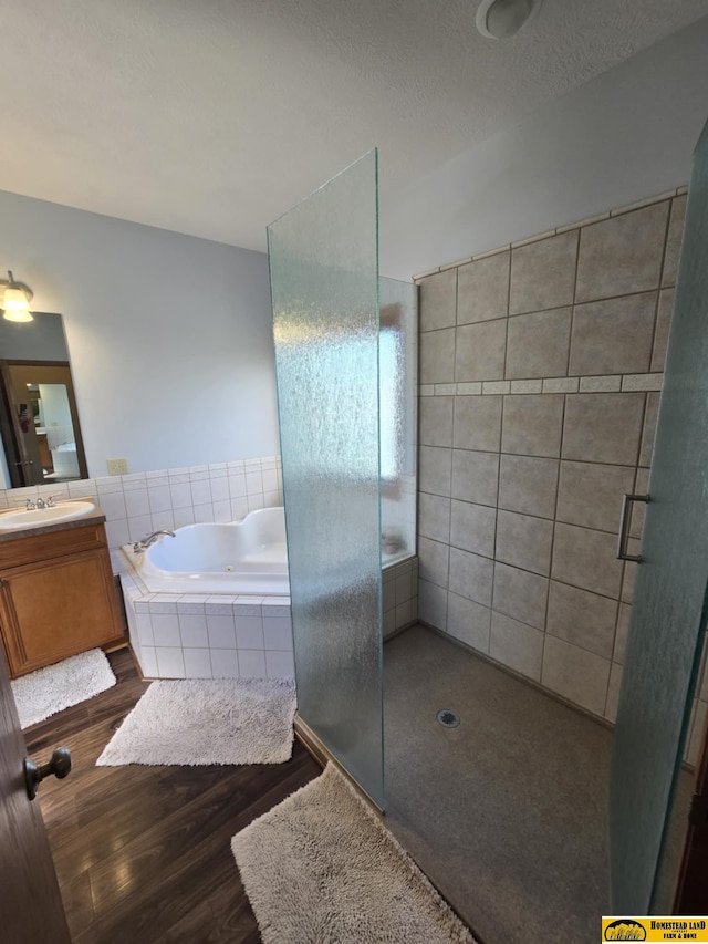 full bath with a textured ceiling, wood finished floors, vanity, tiled shower, and a tub with jets