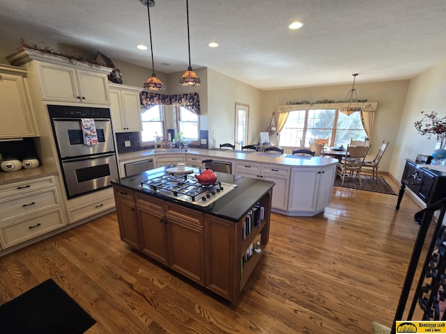 kitchen with a peninsula, plenty of natural light, stainless steel appliances, and dark wood-type flooring