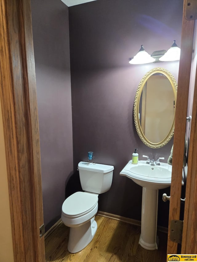 half bath featuring baseboards, toilet, and wood finished floors