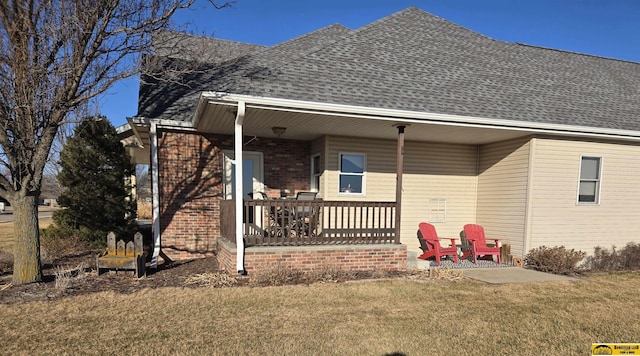 back of property with brick siding, a porch, roof with shingles, and a lawn