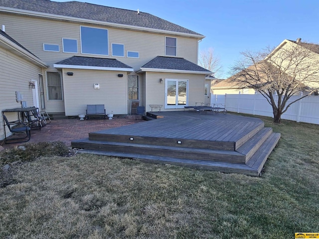 rear view of property featuring a shingled roof, fence, a deck, and a lawn