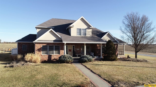 view of front of house featuring covered porch, roof with shingles, brick siding, and a front yard